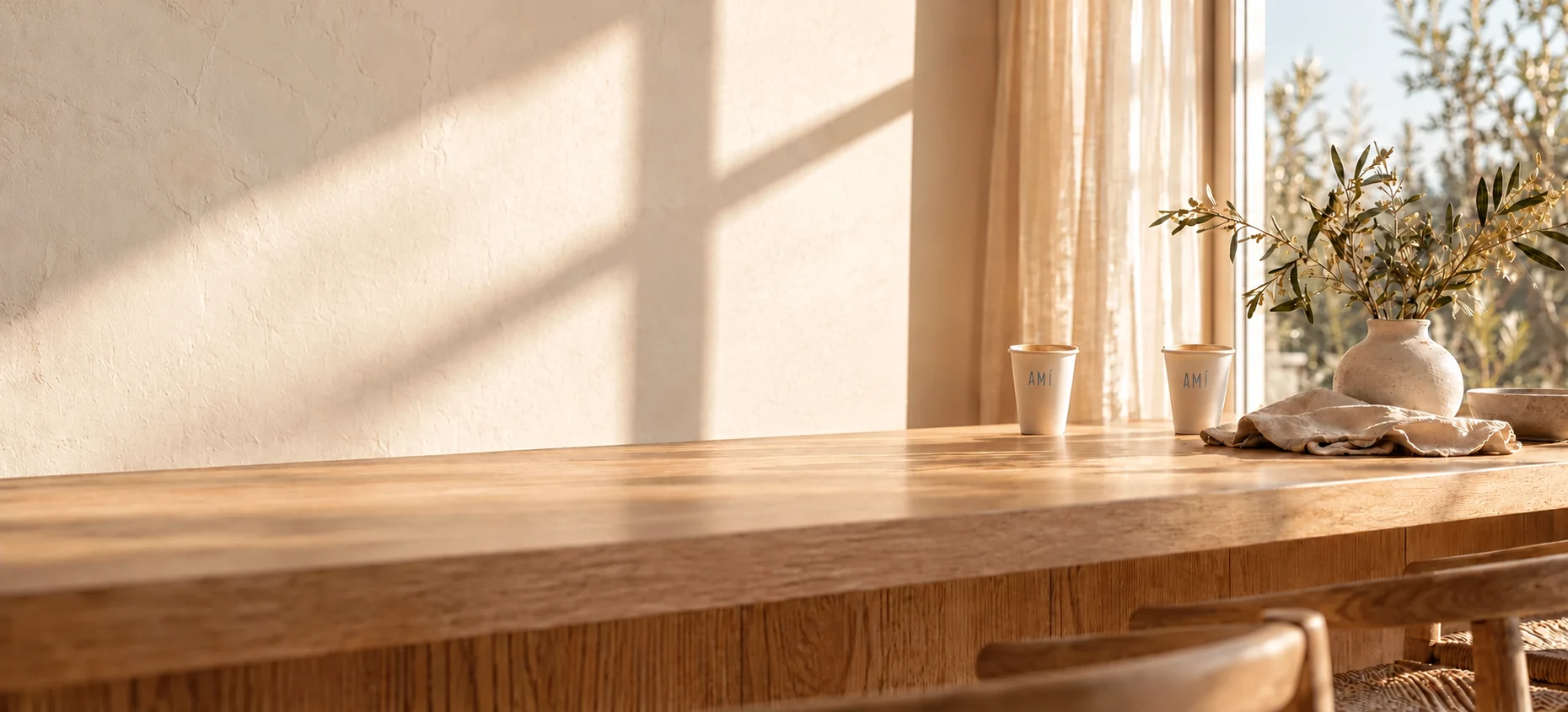 Small, slender AMÍ coffee cups resting in the background of a sunlit oak table